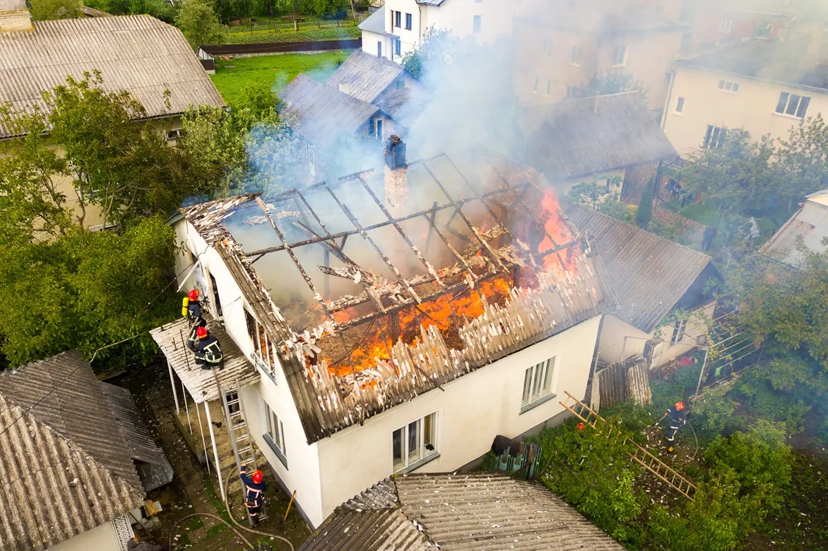 Fire-Restoration Aerial view of firefighters on a ladder spraying a burning roof