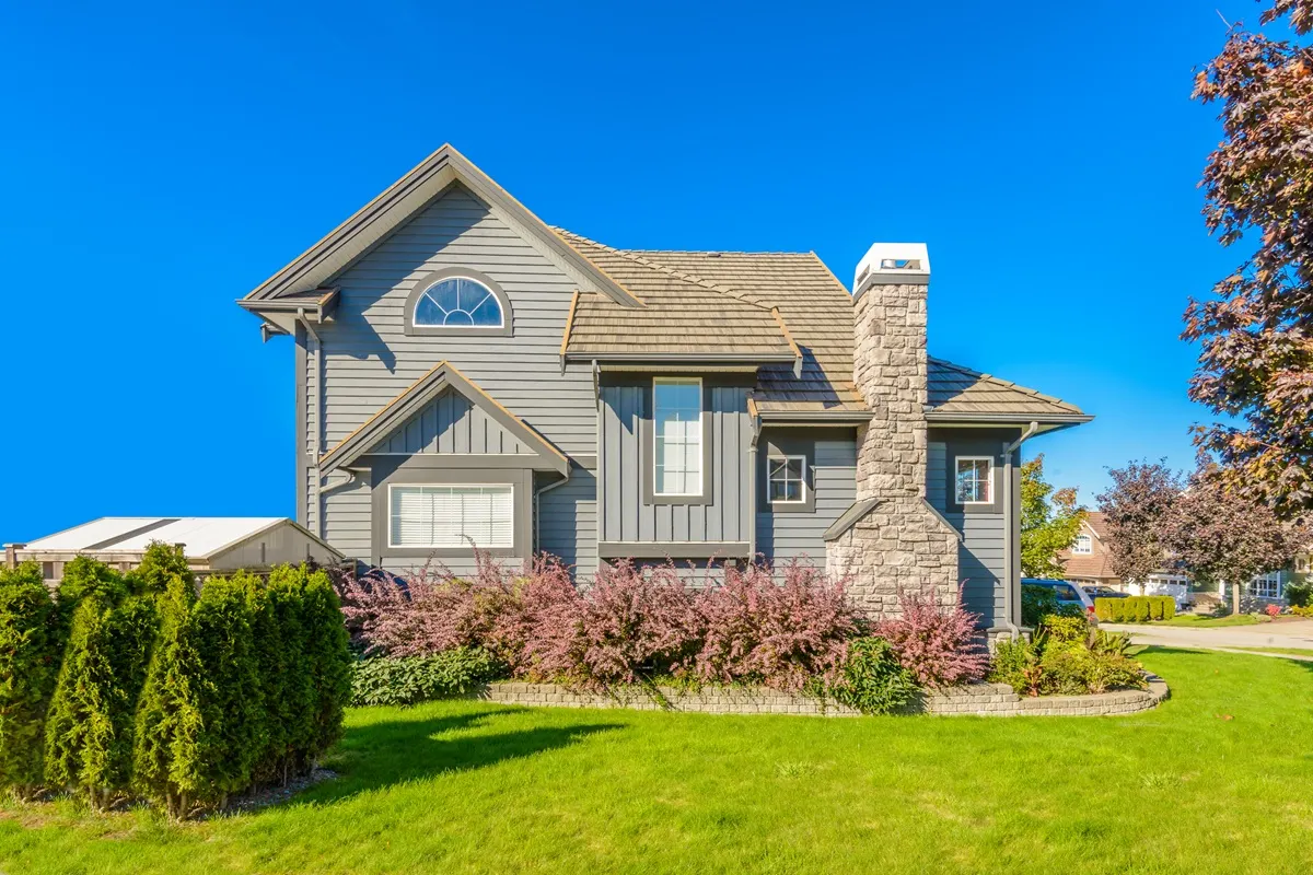 House image The exterior of a green ranch-style house with a stone patio, large windows, and surrounding trees.